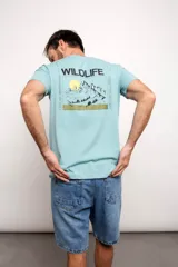 Remera verde agua con estampa en la espalda de montañas, sol y texto 'Wildlife', 'Live an adventure' y 'Trek the mount'.