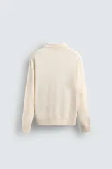 Sweater color crema de punto, con cuello polo y mangas largas. Tejido en hilatura de cáñamo con acabados en rib.
