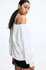 Buzo blanco con escote off-the-shoulder, hombros caídos, corte holgado y mangas largas con puños ajustados.