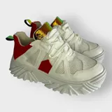 Zapatillas deportivas color crema con detalles en gris y blanco. Presentan una suela gruesa con diseño geométrico y cordones blancos.