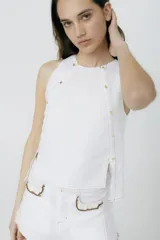 Musculosa blanca de lino con cuello redondo y botones dorados en los hombros y laterales. Tiene aberturas laterales.