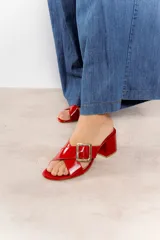 Sandalia tipo zueco de charol rojo con hebilla dorada y taco cuadrado.