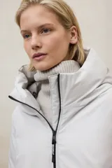 Campera acolchada larga, color blanco, con capucha grande y cierre frontal de cremallera negra. Presenta bolsillos laterales con cremallera negra.