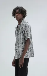 Camisa de manga corta, tejida de punto abierto (símil crochet), color blanco y negro con estampado paisley. Tiene cuello tipo solapa y calce oversize.