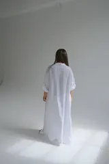 Camisola larga blanca de lino italiano, con corte fluido, cuello camisero, mangas 3/4 con trabilla y dos bolsillos de parche en el pecho.