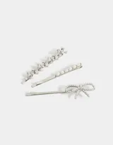 Set de tres horquillas plateadas para el pelo: una con moños de strass, otra con perlas y otra con un moño de strass.