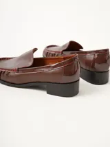 Mocasines de cuero color marrón con apliques de charol y pespuntes rojos.