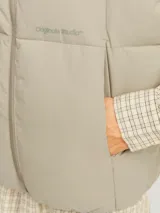 Chaleco acolchado sin mangas color gris topo, con cuello alto y cierre de cremallera. Tiene bolsillos frontales y relleno de fibra sintética.