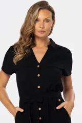 Mono corto negro de lino con cuello camisero, cierre frontal con botones de madera, bolsillos laterales y cinturón del mismo tejido.
