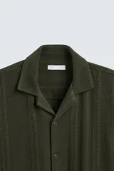 Camisa verde militar de corte relaxed fit, con cuello bowling, manga corta, bajo con aberturas laterales y cierre frontal de botonadura.