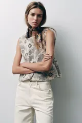 Top sin mangas con estampado de flores blancas y negras, cuello redondo, corte peplum y cierre con botón en la espalda.