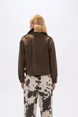 Campera marrón de eco-cuero con cuello de piel sintética negra, cierre frontal con botones a presión, bolsillos con solapa en el pecho y corte holgado.