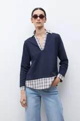 Sweatshirt azul marino de manga larga con cuello en V, superpuesto a una camisa de cuadros beige y azul que asoma en el cuello, puños y ruedo.