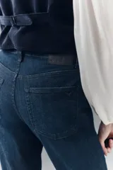 Pantalón de jean de tiro medio, calce ajustado, lavado azul oscuro, pierna levemente acampanada con ruedo ancho.