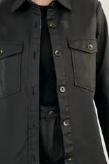 Sobrecamisa negra de textura simil cuero, con cuello camisero, cierre frontal con botones, mangas largas con puños abotonados, dos bolsillos con solapa en el pecho y corte recto.