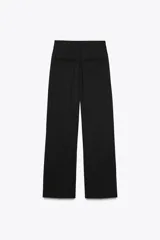 Pantalón negro de tiro medio con trabillas, detalle de pliegue, bolsillos laterales y falsos bolsillos de vivo en la espalda. Cierre frontal con cremallera, botón interior y gancho metálico.
