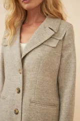 Tapado largo color beige con cuello solapa y corte recto. Cierre frontal con botones, detalles aplicados en la parte delantera, tajo en la espalda y bolsillos ojal con tapa. Con forro. Hecho en Uruguay con tela 100% lana fina sin teñir.