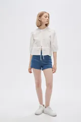 Blusa blanca de algodón con textura de lunares, corte recto, cuello redondo, mangas 3/4 abullonadas y cierre frontal con botones.