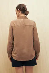 Camisa blanca de manga larga con textura sutil y caída fluida. Presenta cuello clásico, botones forrados a tono y puños con terminación fruncida.