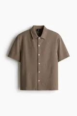 Camisa marrón de punto con textura, corte regular, cuello inglés, tapeta lisa, canesú en la espalda, bajo recto con aberturas laterales y manga corta.
