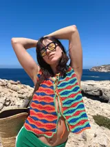 Chaleco tejido a mano en crochet con hilado 100% algodón, con diseño a rayas horizontales en tonos marrón, beige y blanco. Presenta terminaciones en color naranja y lazos del mismo color para cerrar en el frente.