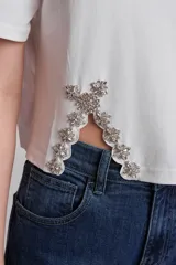 Remera blanca de algodón con cuello redondo y mangas cortas. Presenta apliques de strass en los laterales del ruedo.
