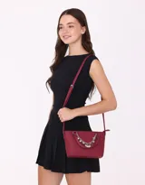 Cartera tipo city de cuerina color bordó, con doble asa corta y correa larga regulable. Incluye charm decorativo con cadena plateada y dijes colgantes.
