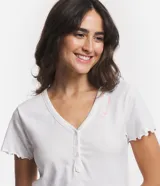 Pijama corto de algodón con blusa blanca de cuello V con botones y mangas cortas onduladas, y short amarillo con estampado de corazones y cintura elástica.
