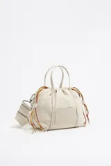 Bolso bandolera pequeño de nylon color crudo, con estructura suave, doble asa de mano y correa de tela ajustable. Detalles en cuero, logo Bimba y Lola grabado, acabado metálico plateado, bolsillo interior y cierre ajustable.