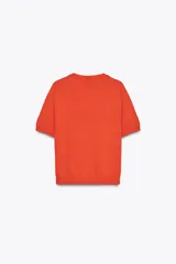Chaqueta de punto color naranja con cuello redondo y manga corta. Presenta cierre frontal con botones y estampado de rombos en tonos blanco, naranja y marrón.