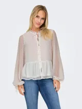 Blusa blanca con textura de lunares, cuello con volantes y lazo, cierre frontal con botones, mangas largas abullonadas con puños elásticos y corte peplum.
