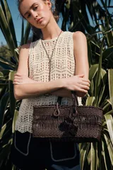 Bolso de mano marrón con cuerpo trenzado y doble asa. Incluye charm extraíble y bolsa interior con cierre fruncido.