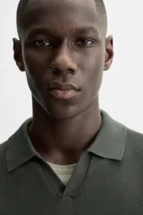 Jersey de punto color verde oliva, de calce relajado (relaxed fit), con cuello solapa y abertura frontal en forma de V. Es de manga corta y presenta acabados en rib en puños y ruedo.