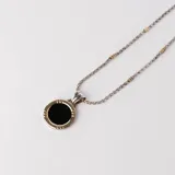 Conjunto de collar con cadena de eslabones plateada con detalles dorados y dije circular con borde dorado y centro de ónix negro.