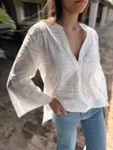 Blusa blanca de algodón con bordado tipo broderie, escote en V y mangas largas acampanadas.