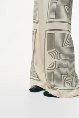 Pantalón de corte recto color crema con estampado geométrico en negro. Modelo de tiro alto con elástico en la parte posterior de la pretina y cierre oculto en un lateral.