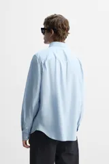Camisa celeste de corte regular fit, confeccionada en popelín de algodón. Tiene cuello abotonado, manga larga con puños abotonados y cierre frontal con botones.