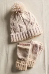 Set de invierno compuesto por un gorro de punto con pompón y guantes mitones con solapa rebatible. Ambas piezas están confeccionadas en un tejido de punto grueso con diseño de ochos y puños acanalados.