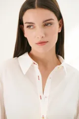 Camisa blanca de manga larga con bordados florales marrones en las mangas.