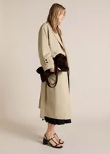Abrigo largo color beige, de corte oversize, con cuello de solapa, doble botonadura, cinturón desmontable y forro interior.