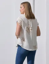 Camisa color beige con estampado de hojas marrones, de manga corta, con cuello a la base con solapa y escote en V.