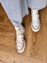 Zapatillas de lona blancas de caña alta con cordones y puntera de goma. Logo de durazno engomado en la base y en la cara interna.