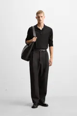 Pantalón negro de corte amplio, con pliegues en la parte delantera, bolsillos laterales y traseros de ojal.
