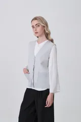 Chaleco de punto color crema, con cuello en V, cierre frontal de botones y dos bolsillos frontales.