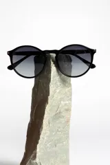 Lentes de sol unisex con montura redonda negra y lentes degradadas de gris a transparente.