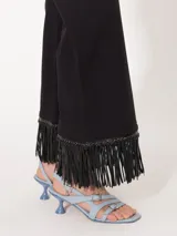 Pantalón negro de twill con corte acampanado y largo hasta el tobillo. El ruedo está terminado con flecos de cuerina al tono.