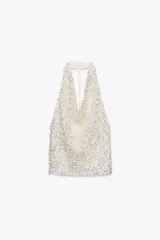 Top blanco con lentejuelas plateadas, de cuello halter y espalda descubierta.