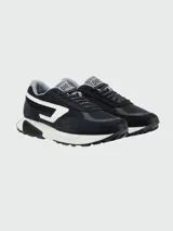 Zapatillas deportivas Diesel modelo S-Tyche D, color negro con detalles en blanco y gris. Presentan una silueta de running retro con paneles de malla y gamuza, entresuela gruesa blanca y suela exterior negra. El logo lateral es una 'D' estilizada en blanco.