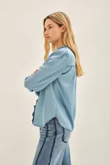 Camisa celeste de tencel con calce recto, cuello redondo con volados, canesú en delantero y espalda, y mangas largas terminadas en puño con botón snap.