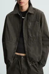 Cazadora color verde oscuro de corte relaxed fit, confeccionada en tejido técnico. Tiene cuello solapa, manga larga con puño abotonado, bolsillos plastrón en el delantero y bajo ajustable con elástico en los laterales. Presenta efecto lavado y cierre frontal con cremallera oculta por solapa con botones a presión.